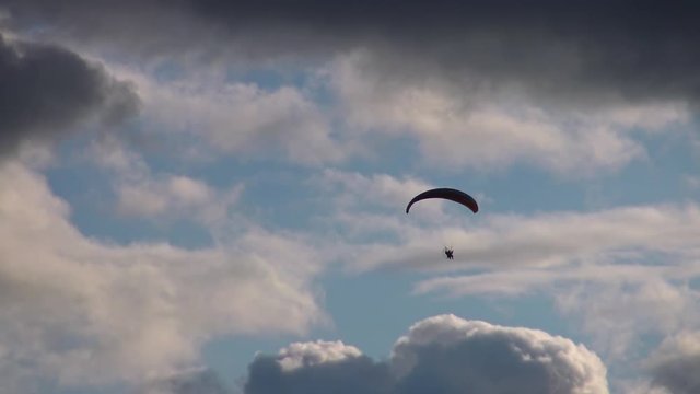 Paraglider flying high in the clouds. Air sport and recreation. A powered paraglider - a glider with a dorsal power plant, providing the rise and moving in the air.