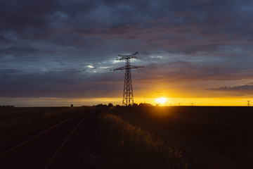High voltage power lines and transmission towers at sunset. Poles and overhead power lines silhouettes in the dusk. Electricity generation and distribution. Electric power industry and nature concept