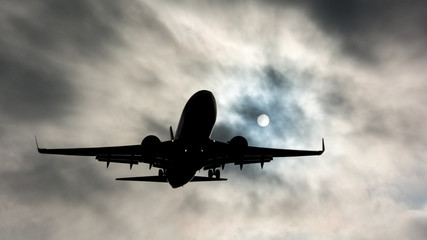 Silhouette of a plane in the clouds with the sun in LAX