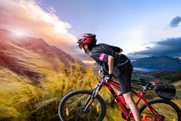 Naklejka premium strong woman riding moutain bike upon the hill with strong windy impact through the on the moutain, river and moutain in background