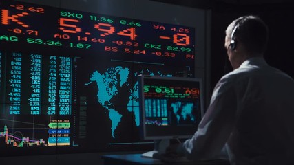 Adult man working in office of exchange and driving lively trade while speaking with headset. - Powered by Adobe