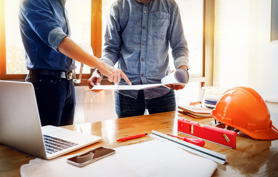 A young engineer pointing blueprint and use laptop to explaining the design to the foreman, so that Foreman brings the house design team to the customer's needs at work. Architecture design concept.