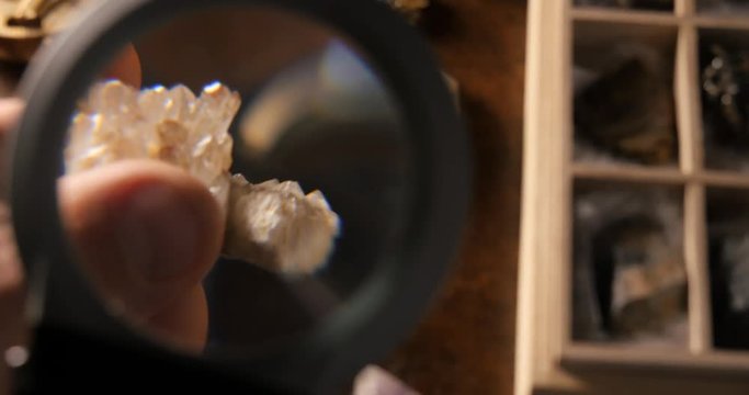 Geologist hand examines rock crystals mineral under magnifying glass