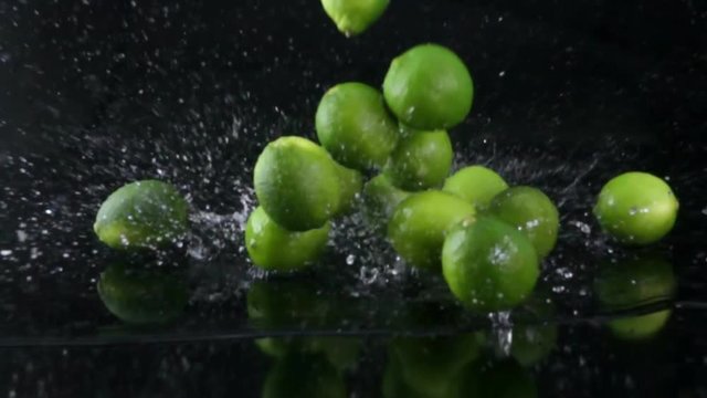 Limes falling with water on black background in slow motion