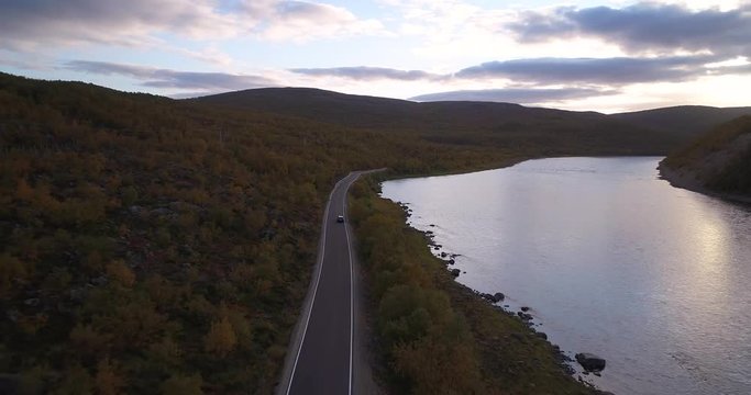 Autumn color road, Cinema 4k aerial view following a car driving on road 970 the tenontie, near tenojoki river, at the border of norway and utsjoki, on a sunny evening dawn, in Lapland, Finland