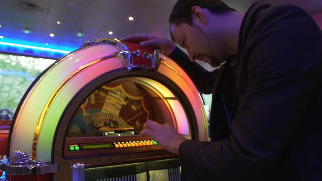 Cheerful man selecting song on vintage music box, having fun in bar, party