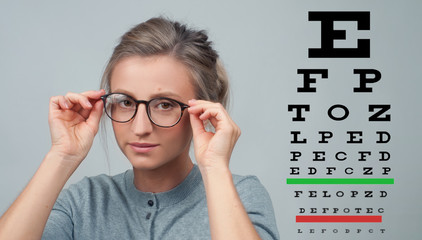 Eyesight check. Woman in glasses on the background of eye test chart