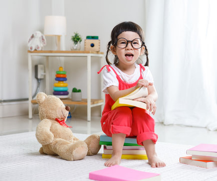 Preschooler girl learns at school. Cute child reading with teddy bear. Little girl having fun indoors at home, kindergarten or