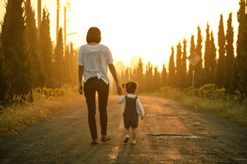 Happy family in the park evening light. The lights of a sun. Mom and baby happy walk at sunset. The concept of a