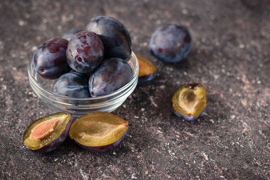The fruits of ripe blue plums in a glass bowl on the stone table.