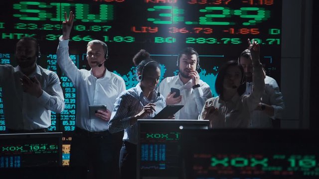 An enthusiastic stock broker team in a futuristic office full of live global market feeds.