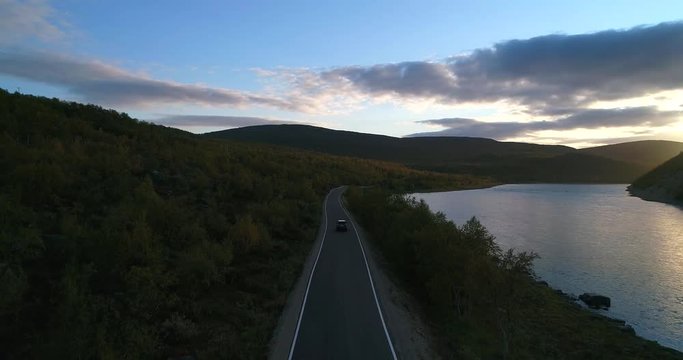 Car on a autumn color road, Cinema 4k aerial view above a auto driving on road 970 the tenontie, near tenojoki river, on a sunny evening dawn, in Lapland, Finland
