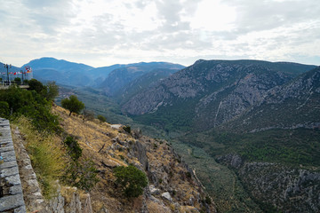 View of Parnassus limestone mountain valley, green olive groves and other trees with bright sky background and many of national flag poles upon hill