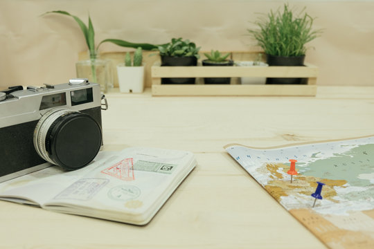 camera, passport,  world map with pins 2 pieces point on map placed on wooden table has plants in vase are background. this image for business, travel, photography, equipment, map concept
