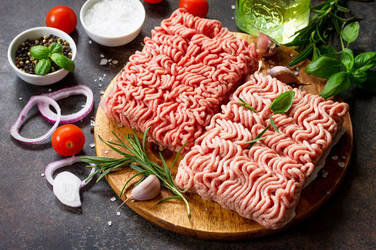 Minced beef and pork on a cutting board, raw meat and various spices on a stone or slate background.