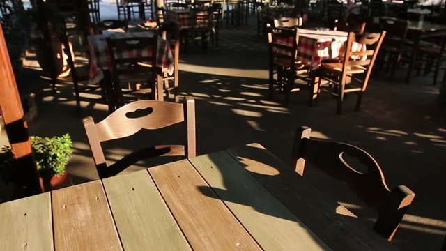 Chairs and tables in typical outdoor Greek tavern in morning sunlight with shadows.
