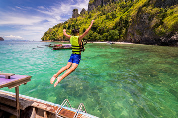 Young man traveler jump into the sea form long thai boat at Chicken island near Railay beach in...