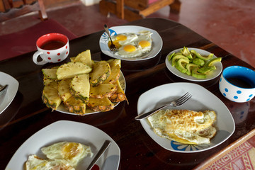 Breakfast table with fried eggs, scrambled eggs, pineapple, avocado, coffee