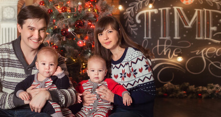 Merry Christmas and Happy New Year 2018 Holidays concept. Cheerful mom, dad and cute twins baby boys smiling. Parents and two little children having fun and playing together near Christmas tree