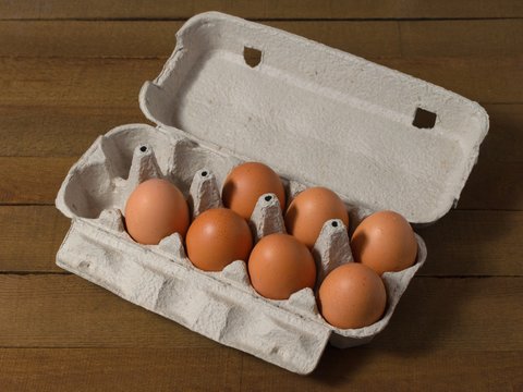 Cardboard box with chicken eggs on a wooden table.