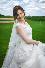 Attractive young bride in a stylish white dress dancing on a green meadow in the nature
