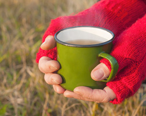 A cup of hot tea in female hands, outdoor.