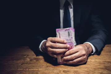 Businessman holding money, Indian Rupee currency, at the table in dark room