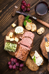 Assorted cheeses on wooden boards plate, grapes, bread wine and pate on dark wooden background, top view, flat lay.