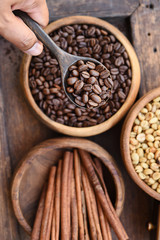 Close up of coffee beans in wooden bowl and cinnamon on wooden background