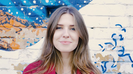 Happy young woman standing front of brick wall, looking at camera. Young attractive woman looking at the camera on the street near the wall