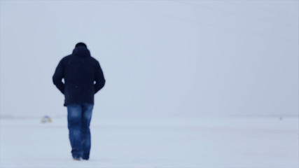 Man walking in snow. Man walking on snow, footprints in snow, behind. Man walks in the winter in the field