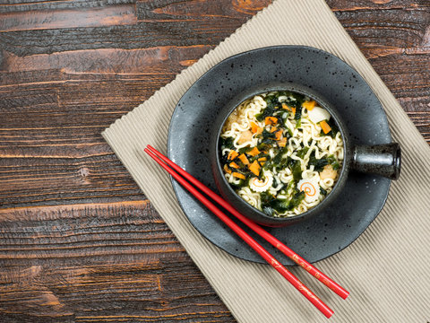 Bowl of healthy fresh vegetables with Asian noodles served with chopsticks in a bowl in a top down view over a rustic wooden table, with copy space