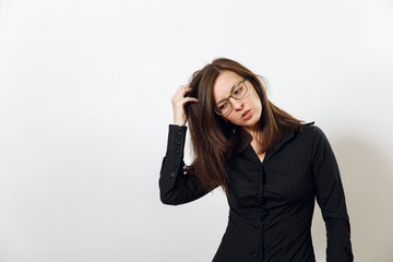 Pretty European worried and pensive brown-haired woman in glasses for sight and headache, dressed in dark black shirt lost in thought and conjectures, on a white background. Emotions concept.