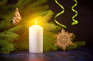 Christmas still life of a burning white candle on the background of fir tree branches and snowflakes toy and bumps. Green serpentine.
