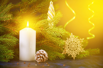 Christmas still life of a burning white candle on the background of fir tree branches and snowflakes toy and bumps. Green serpentine in the background.