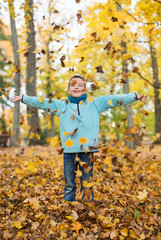 Adorable happy kid playing with fallen leaves in autumn park