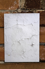 White cracked torn paper pasted to a brick wall.