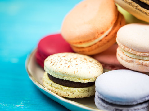 Traditional brightly colored French macaroons on a hand-made plate, set on a blue wooden board, close-up view