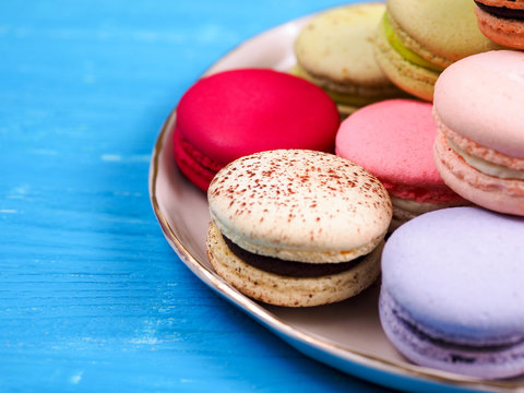 Traditional brightly colored French macaroons on a hand-made plate, set on a blue wooden board, close-up view, selective focus