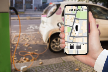 Hand with phone on a background of electric cars charging point. E-car sharing concept