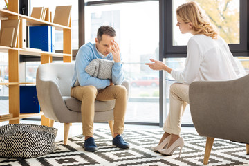 Difficult decision. Cheerless depressed unhappy man holding his forehead and thinking about the...
