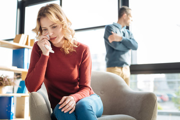 Bad mood. Sad cheerless crying woman sitting in the armchair and holding a paper tissue while feeling depressed