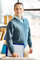 Professional therapist. Handsome positive nice man smiling and looking at you while holding his notes