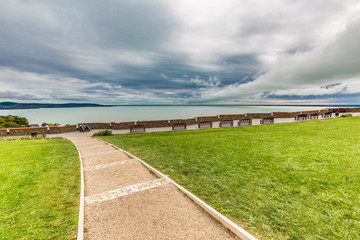 Fototapeta na wymiar Park with lake view. Bench with walk path and cloudy sky