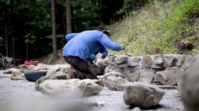 Using a tuckpointing trowel a hardscape smooths out the mortar in a rock wall being built.