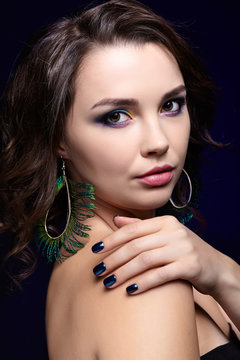 Portrait of beautiful brunette woman on black background and peacock feather earrings