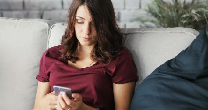 Close-up of a young serious beautiful woman using the phone sitting on the couch in home message smartphone apartment, cellphone communication internet sms typing Slow Motion Shot on RED EPIC camera