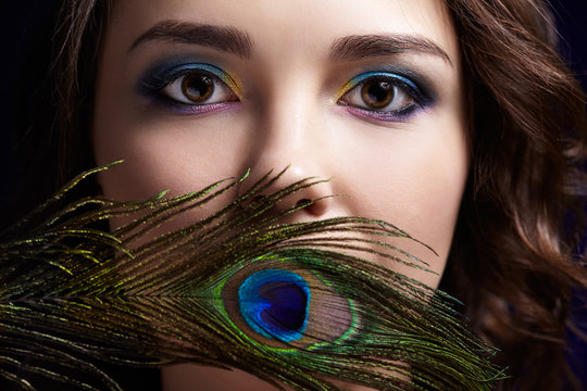 Portrait of beautiful brunette woman on black background and peacock feather