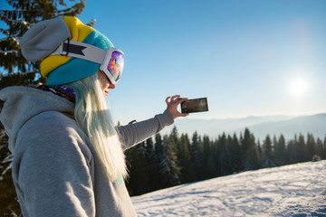 Shot of a female snowboarder using her smart phone while resting after snowboarding, taking photos...