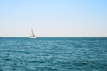 Fototapeta premium Sea lake ocean water landscape with dark waves and a lonely white yacht at the horizon on sunny day.